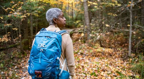 woman walking through forest wearing backpack